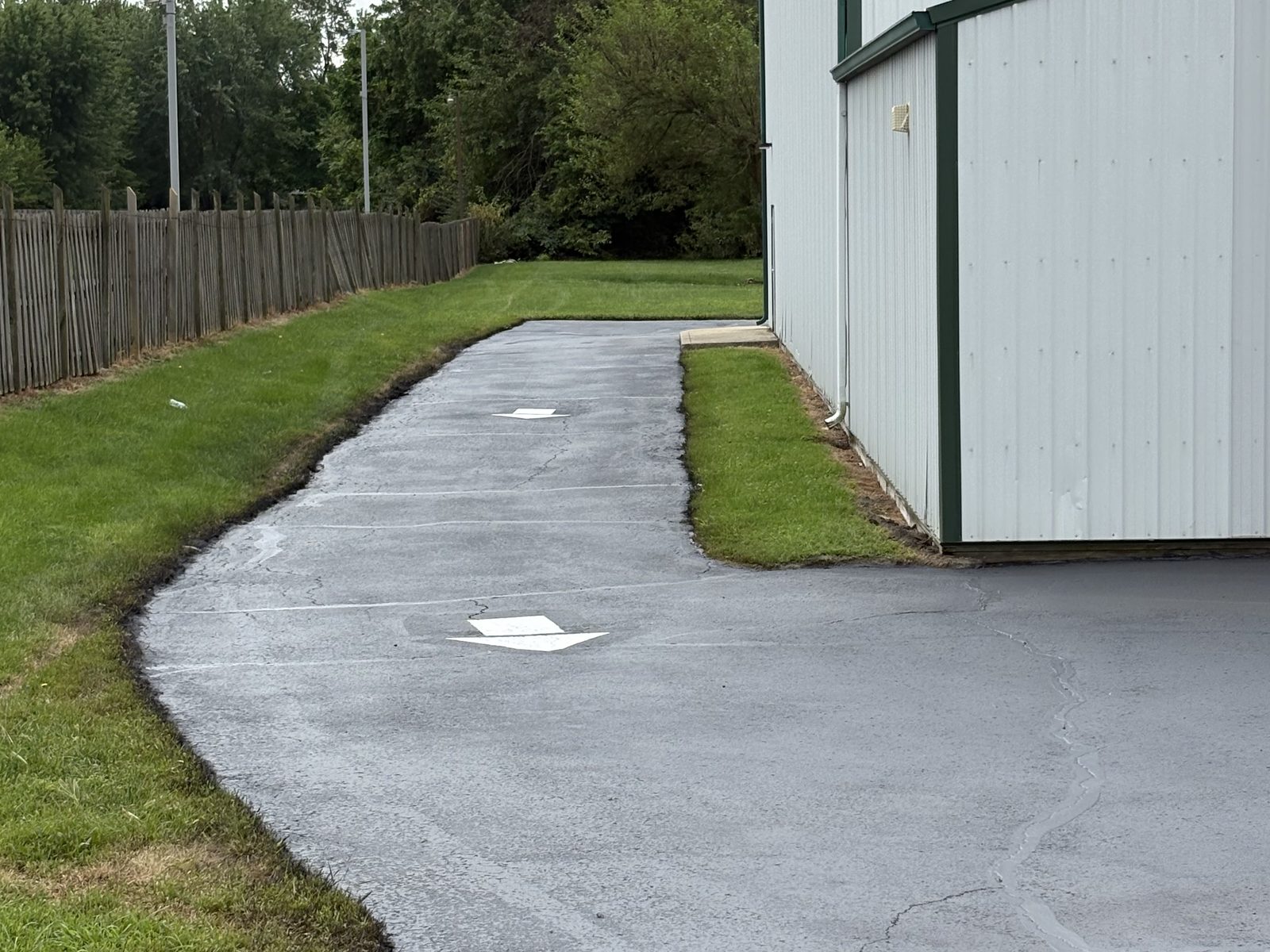 Freshly sealed commercial drive lane running alongside a metal building