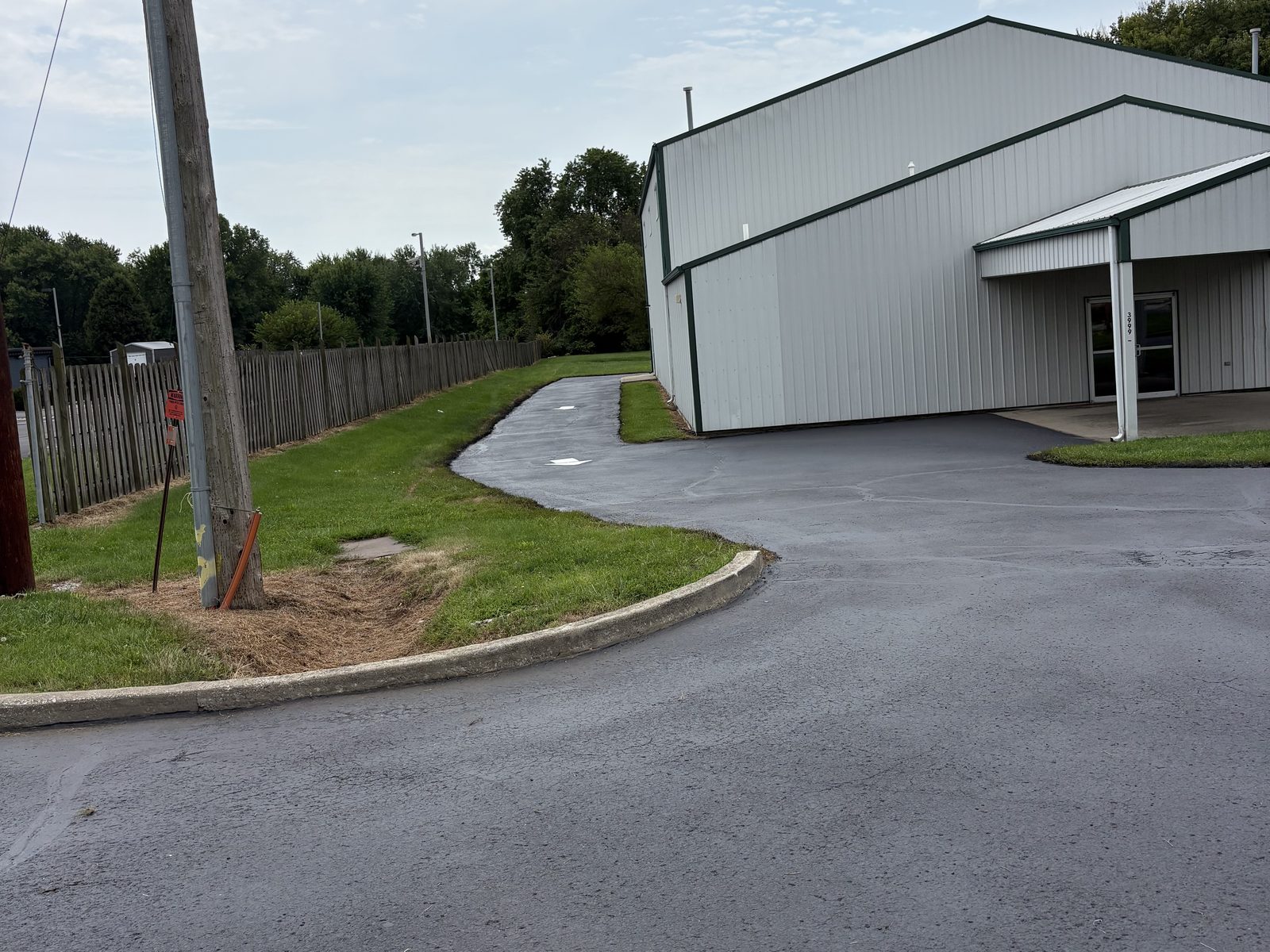 Freshly sealed asphalt drive curving around a commercial pole barn property